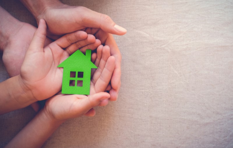 Vantagens do wood frame | Foto das mãos de duas pessoas segurando uma casinha de papel | Método Construtivo | Blog Alea