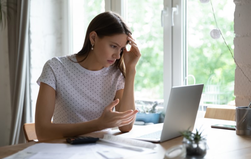 O que acontece se não pagar o IPTU | Foto de uma jovem mulher preocupada olhando para o computador | Como comprar uma casa | Blog Alea