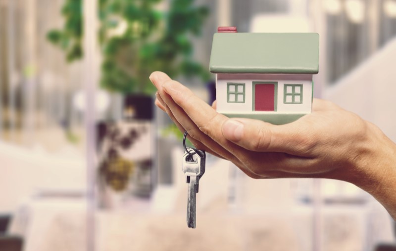 Mão masculina segurando chaves e uma casa de brinquedo | Qual é melhor: condomínio fechado ou apartamento | Como comprar uma casa | Blog Alea