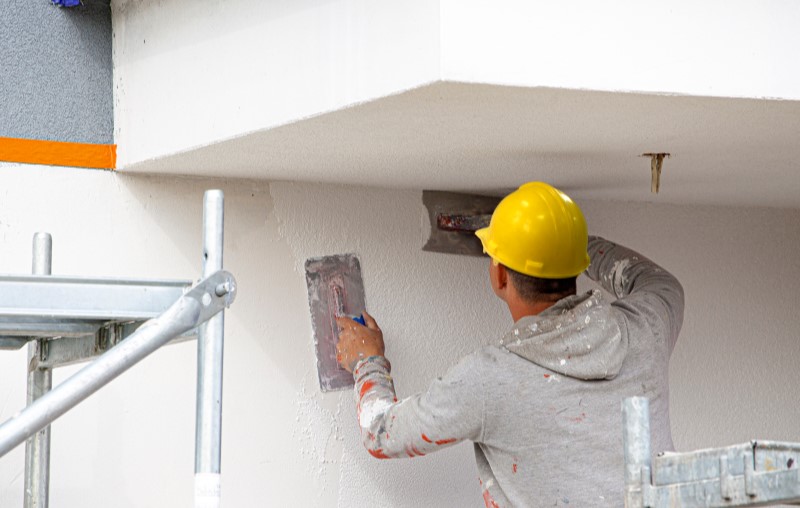 Qual a diferença entre a parede de drywall e a parede de wood frame | Foto de um construtor passando gesso nas paredes | Método Construtivo | Blog Alea