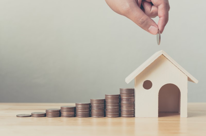 Quais são os outros benefícios do programa | Foto de um fileira de moedas organizadas, com uma mini casinha na ponta e uma mão segurando uma moeda | Blog da Tenda