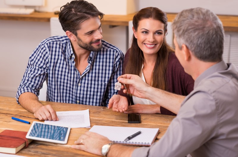 Quando surgiu a profissão de corretor de imóveis | Foto de um agende de vendas vendendo um imóvel para um casal | Como comprar uma casa | Blog da Alea