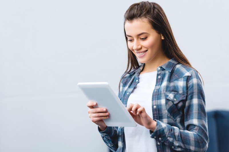 Quais são os benefícios para as faixas de renda do Minha Casa Minha Vida | Foto de um mulher sorridente utilizando um tablet | Tudo sobre Minha Casa Minha Vida | Blog Alea