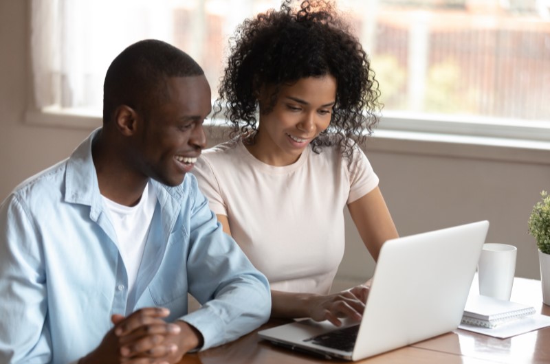 Como o Minha Casa, Minha Vida ajuda na compra da casa própria? | Foto de um casal sorrindo e pesquisando no notebook | Minha Casa Minha Vida | Blog Alea