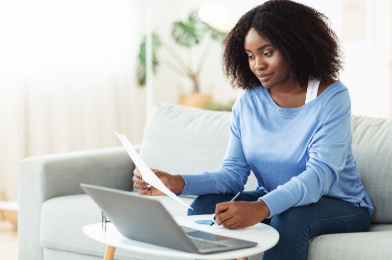 Como participar do Minha Casa, Minha Vida? | Foto de uma mulher segurando um papel e olhando para o notebook | Minha Casa Minha Vida | Blog Alea