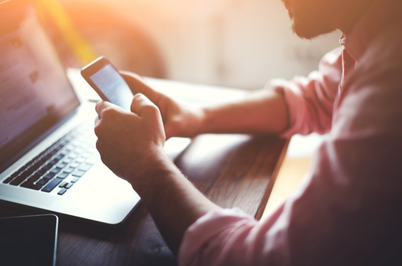 Dúvidas frequentes sobre o programa do Governo | Foto de uma pessoa em frente a um notebook, enquanto usa o celular | Blog Alea