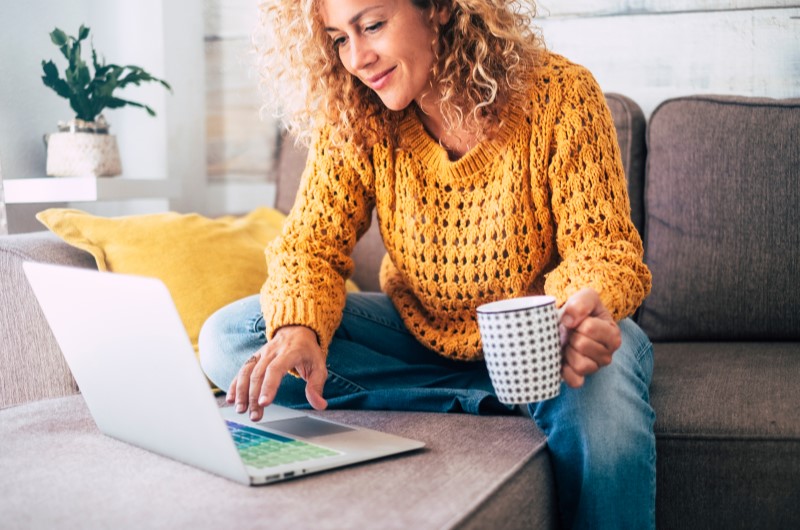 Onde fica a cidade de Assis? | Foto de uma mulher em um sofá, enquanto segura uma caneca e usa o notebook | Estilo de vida | Blog Alea