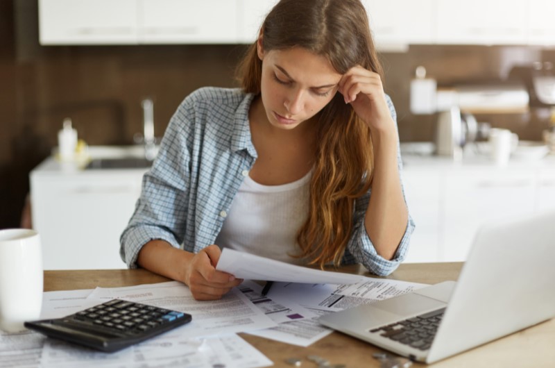 Taxa de juros do programa do Governo | Foto de uma mulher olhando alguns papeis, com uma calculadora e notebook sobre a mesa | Blog Alea