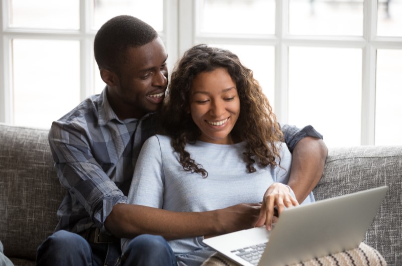 Como escolher a melhor cidade próxima a São Paulo para morar | Foto de um casal sorridente sentado no sofá enquanto utiliza o notebook | Estilo de Vida | Blog Alea