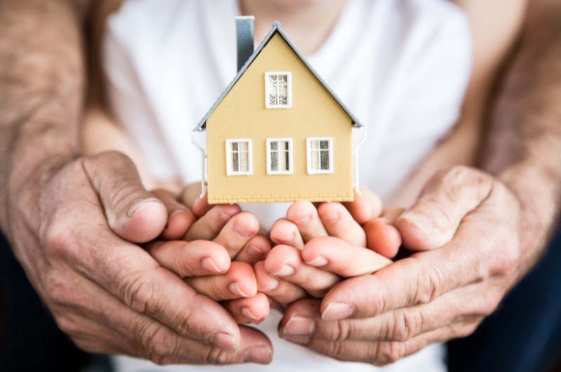 Conheça as 6 melhores cidades próximas a São Paulo para morar | Foto de uma família de mão unidas na frente do corpo, segurando uma miniatura de casinha | Estilo de Vida | Blog Alea