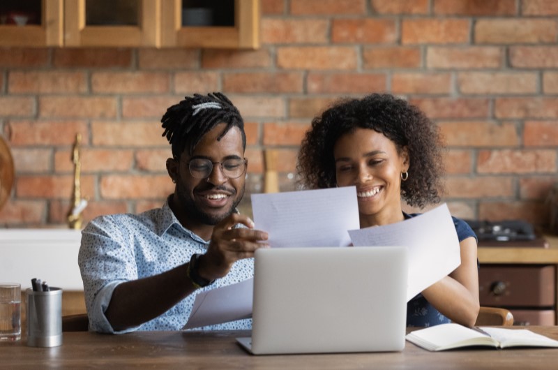 Quais são os tipos de financiamento habitacional Caixa? | Foto de um casal sorridente analisando alguns documentos | Como comprar uma casa | Blog Alea