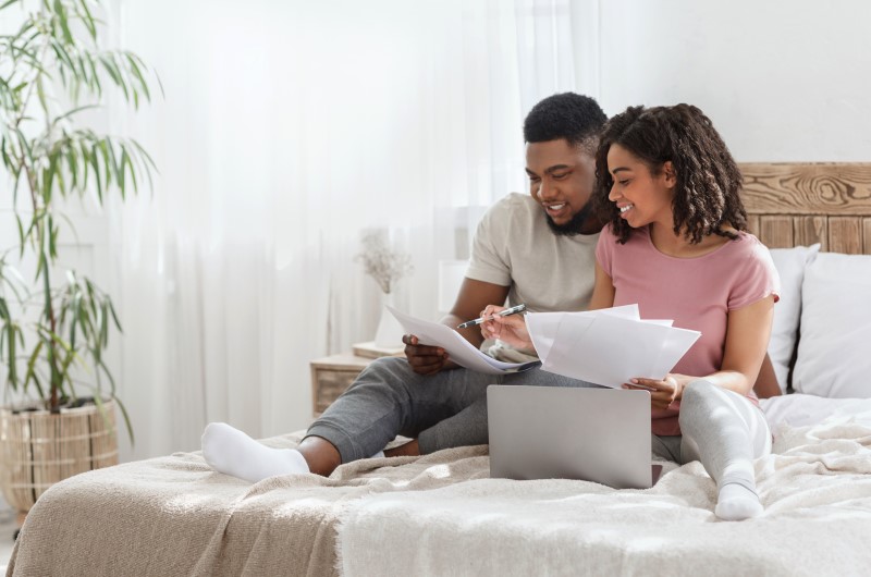 Quem pode financiar com a Caixa? | Foto de um casal usando o notebook e analisando alguns papeis | Como comprar uma casa | Blog Alea