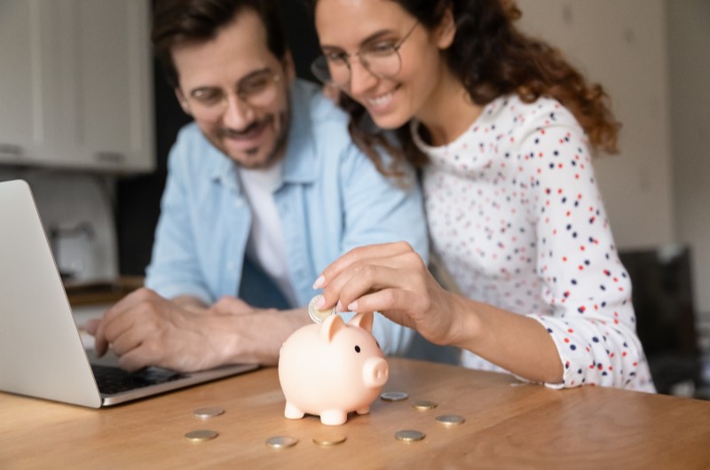 Subsídio | Foto de um casal feliz colocando moedas em um cofrinho | Como comprar uma casa | Blog Alea