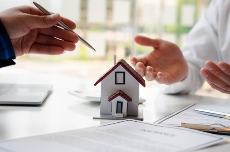 6 motivos para comprar uma casa | Foto de uma casinha, papeis sobre a mesa e a mão de duas pessoas | Como comprar uma casa | Blog Alea