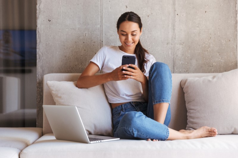 Valorização do imóvel ao comprar uma casa | Foto de uma moça no sofá enquanto usa o celular | Como comprar uma casa | Blog Alea
