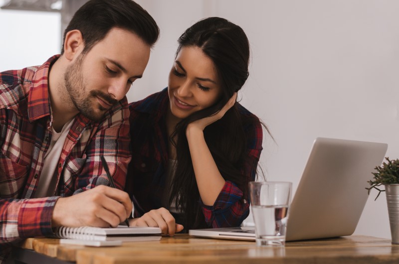 FGTS | Foto de um casal escrevendo em um caderno, com um notebook na frente | Foto de uma pessoa segurando o celular e digitando no notebook | Blog Alea